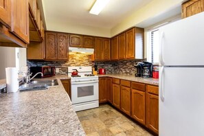 A kitchen with wooden cabinets, a granite countertop, a stove, and a refrigerator.
