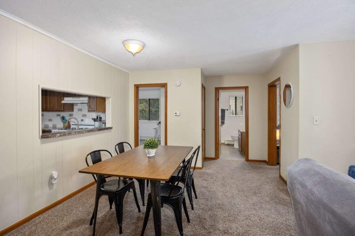 Un comedor con una mesa y sillas de madera, una cocina al fondo y un pasillo que conduce a otras habitaciones.