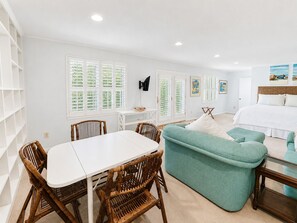 A room with a dining table, chairs, a sofa, a bed, and artwork on the walls.