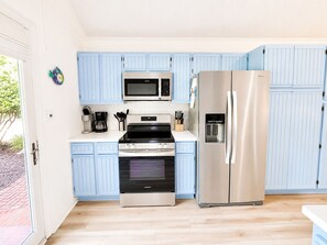 A kitchen with light blue cabinets, a stainless steel refrigerator, a microwave, a stove, and a coffee maker.