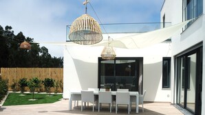 Een modern terras buiten met een eettafel en stoelen, een hanglamp en uitzicht op het aangrenzende gebouw.