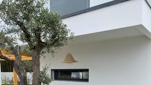 Een modern gebouw met een witte gevel, een grote boom en een klein raam.