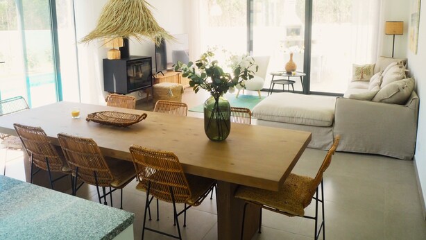 Een ruime woonkamer met een houten eettafel, rieten stoelen, een bank en een televisie.