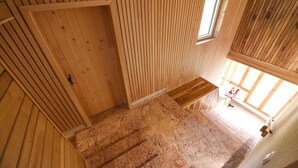 Un interior de madera con una escalera, un ventanal pequeño y una puerta.