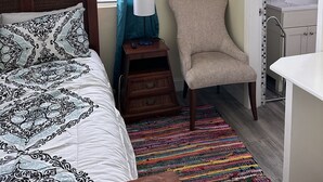 Ein Schlafzimmer mit einem Bett, einem Sessel, einem farbenfrohen Teppich, einem Gemälde eines Löwen und einem Badezimmer mit gefliestem Duschbereich.