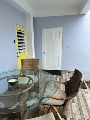 Une table à plateau en verre, des chaises en osier, une porte jaune et une porte blanche dans une pièce aux murs bleu clair.