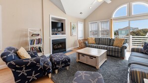 A living room with a fireplace, a television, and a large window with blinds. - Pirate's Booty: Private Pool | Hot Tub | Elevator (Nags Head)