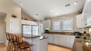 A kitchen with white cabinets, a granite countertop, and a bar stool area. - Pirate's Booty: Private Pool | Hot Tub | Elevator (Nags Head)