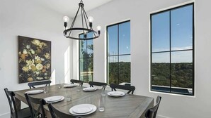 Ein Esszimmer mit großem Tisch, Stühlen, einer Chandelieber und großen Fenstern mit Blick.
