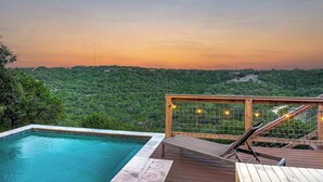 Ein Pool mit Holzterrasse, Glasgeländer und Blick auf eine bewaldete Landschaft.