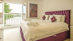 A bedroom with a large bed, a balcony, and a view of greenery.