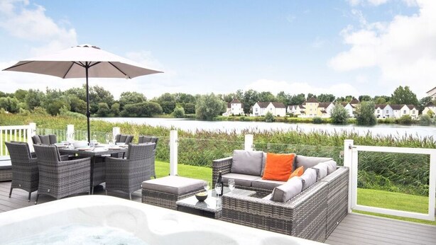 A deck with wicker furniture, a hot tub, and a view of houses across a lake.