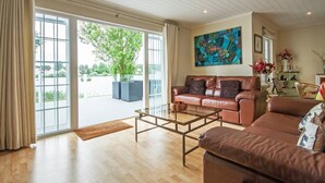 A spacious living room with a leather sofa, a glass coffee table, and a large window with a view of greenery outside.