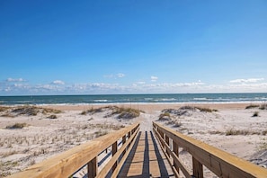 A wooden boardwalk leading to a beach with sand dunes and the ocean in the background.