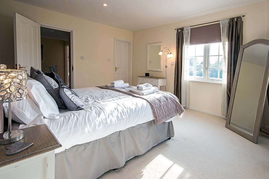 A bedroom with a bed, bedside table, lamp, mirror, and window with curtains.