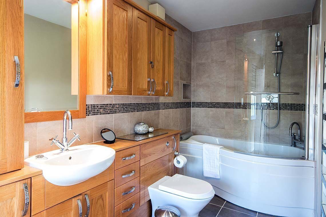 Une salle de bain moderne avec un meuble-lavabo en bois, un lavabo blanc, des toilettes et une douche séparée par une paroi en verre.