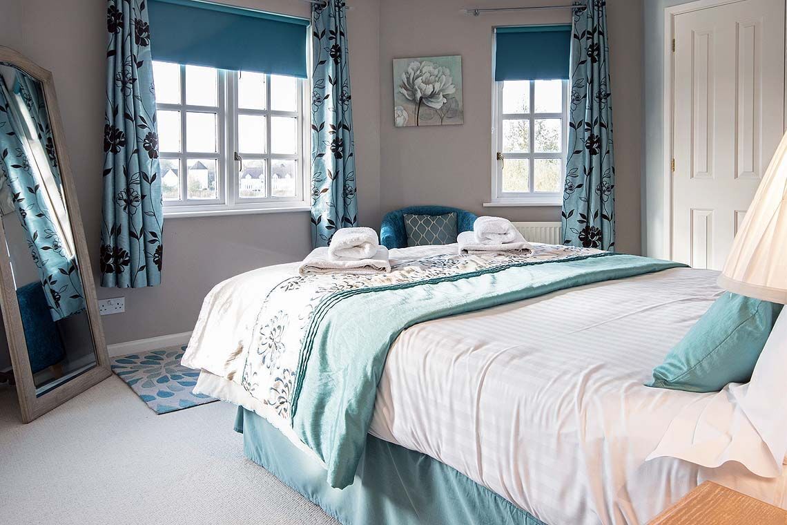 A bedroom with a bed, two windows, a mirror, and a door.