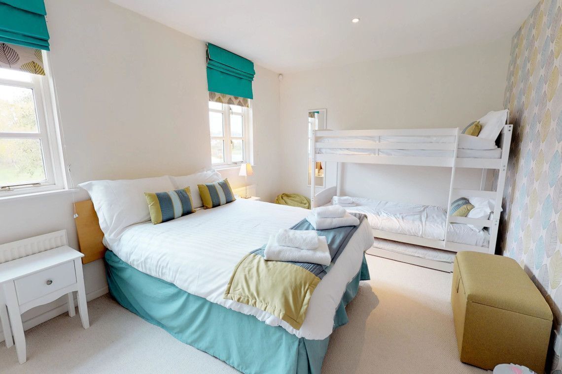 A bedroom with a bunk bed, a bedside table, a chair, and a window with curtains.