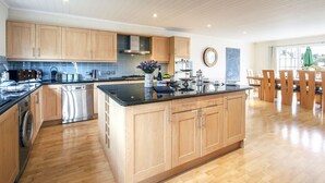 A modern kitchen with wooden cabinets, a stainless steel dishwasher, and a large island with a black countertop. - Windrush Lake 80/81, Waterlow Lodge (P) - Lakeside Lodge, Hot Tub, Sleeps 7 (South Cerney)