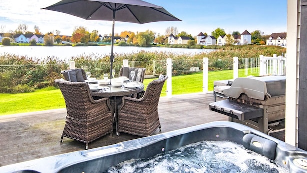 Une terrasse dotée d’un jacuzzi, de mobilier d’extérieur et offrant une vue sur un lac et des maisons.