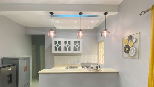 A modern kitchen with a central island, pendant lights, and a decorative wall piece.