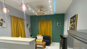 A modern kitchen with a central island, a dining area with a sofa and table, and a living room with a sofa and curtains.