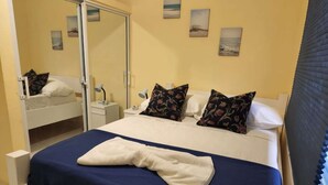 A neatly made bed with a blue and white bedspread, two pillows with floral patterns, a bedside lamp, and a nightstand with a lamp.