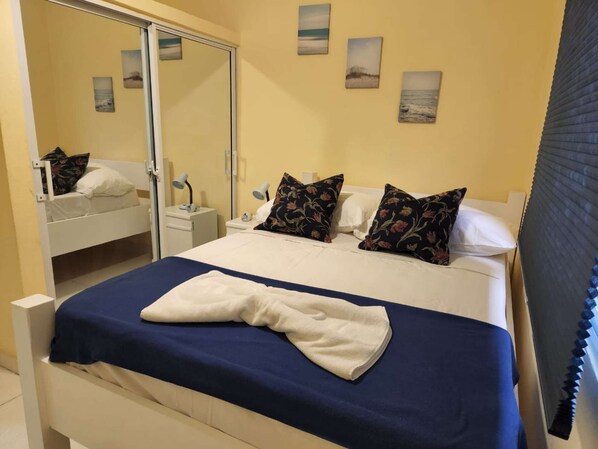 A neatly made bed with a blue and white bedspread, two pillows with floral patterns, a bedside lamp, and a nightstand with a lamp.