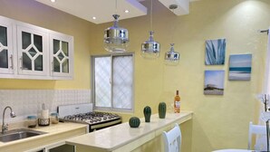 A kitchen with white cabinets, a gas stove, a sink, and a window with frosted glass. There are three hanging pendant lights and a cactus on the counter.