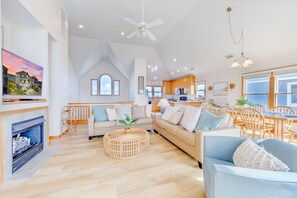 A spacious living room with a fireplace, a large sofa, a dining area with wooden chairs, and a kitchen in the background. - Soundfront Dog Friendly w/ Hot Tub, Windsports Access, Community Pool and Dock (Avon)