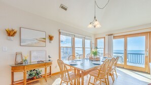 Un comedor con una mesa grande, sillas de madera y vista al mar a través de amplios ventanales.