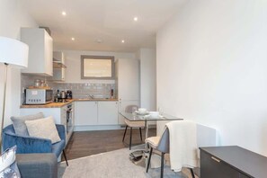 A compact kitchen with modern appliances, a dining area with a glass table, and a cozy seating area with a sofa and armchair.