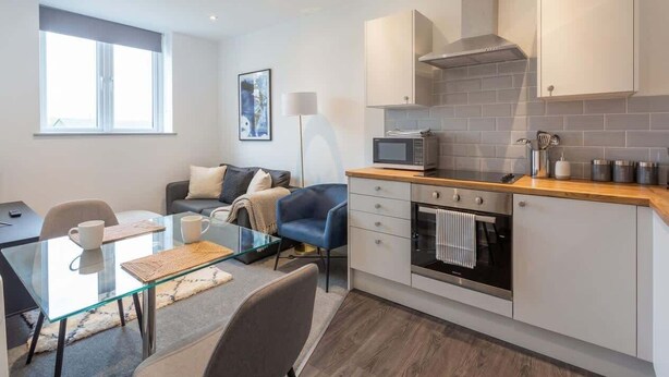 Una cucina moderna con forno a microonde, forno e pensili, un tavolo da pranzo in vetro con sedie e un divano nella zona living.