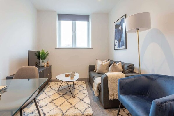 A modern living room with a sofa, a blue armchair, a glass coffee table, a dining table, and a floor lamp.