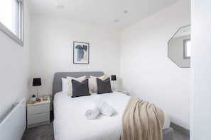 A hotel room with a bed, a nightstand, a lamp, a towel, and a framed picture on the wall.