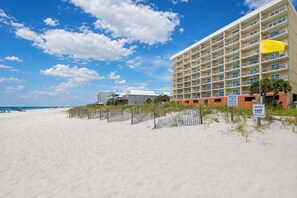 Un hotel frente a la playa con varios balcones, una playa de arena y cielo despejado.
