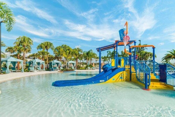 Een waterpark met een blauwe en gele speelstructuur, palmbomen en ligbedden.