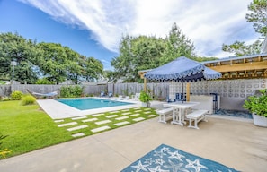 A backyard with a swimming pool, a covered patio area, and a wooden deck.