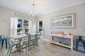 A dining area with a wooden table and chairs, a chandelier, and a wall-mounted painting.
