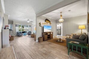 A spacious living room with a television, a chandelier, and a dining area with a table and chairs.