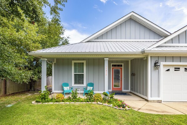 A single-story house with a front porch, two chairs, a red door, and a garage.