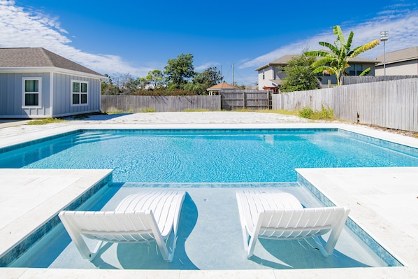 Relax by the rectangular pool surrounded by a white tiled deck and lounge chairs.