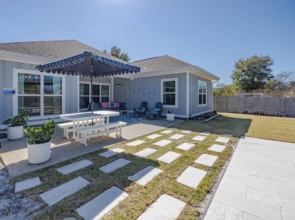 A house with a covered patio, a swimming pool, and a lawn with stepping stones.