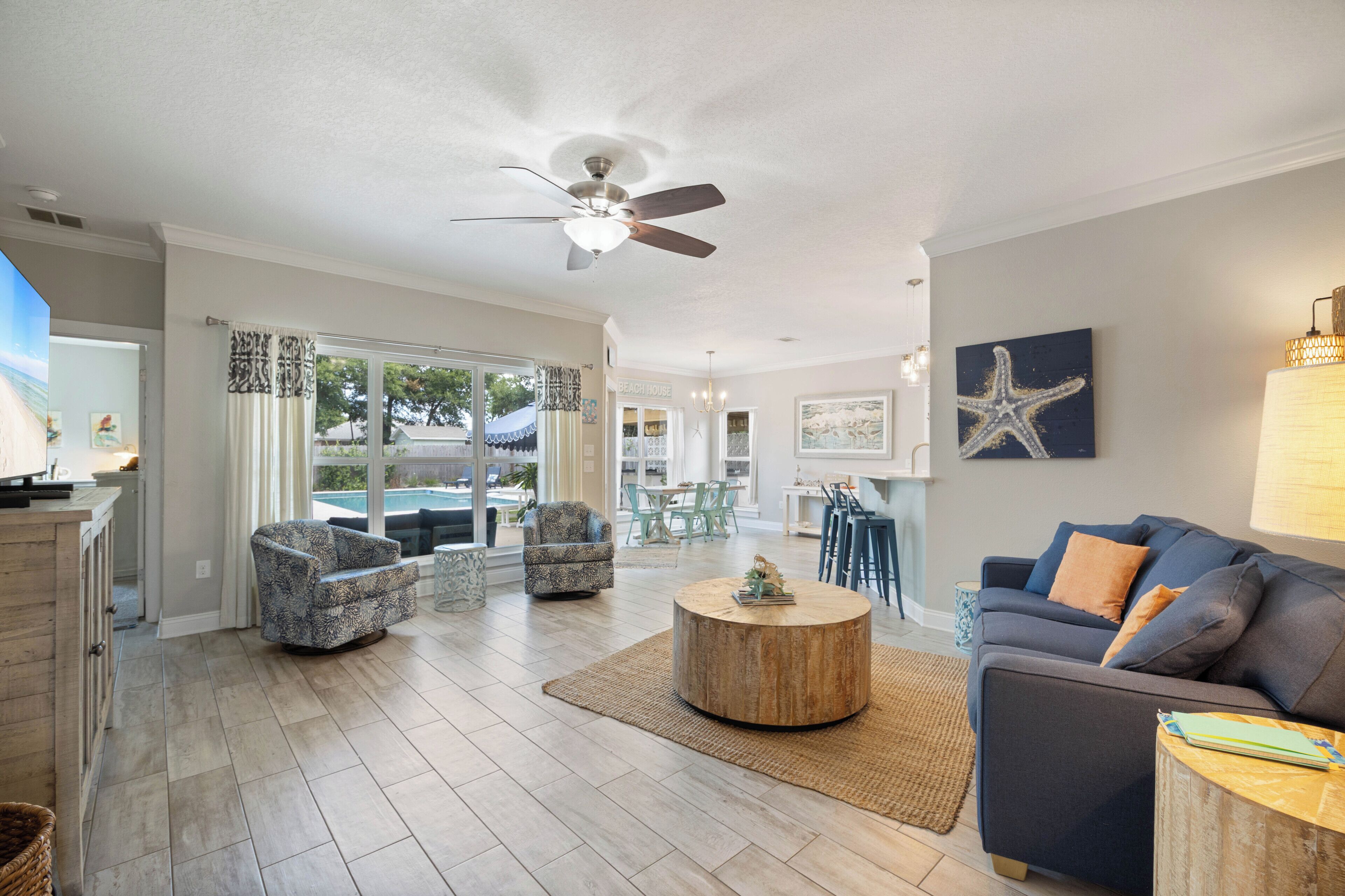 A spacious living area with a ceiling fan, a round wooden coffee table, and a blue sofa with orange cushions.