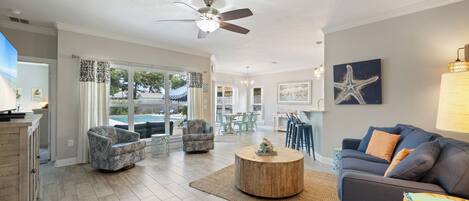 A spacious living area with a ceiling fan, a round wooden coffee table, and a blue sofa with orange cushions.