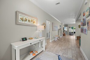 Un couloir avec une console blanche, un tableau encadré représentant des pélicans et une lampe décorative.