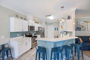 A modern kitchen with white cabinets, a central island with bar stools, and a view to the dining area.