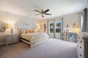 A bedroom with a bed, a desk, a chair, a ceiling fan, and a window with curtains.