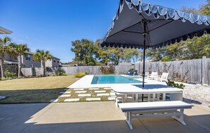 A backyard with a swimming pool, a covered patio area, and a wooden fence.