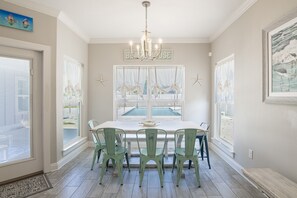 Enjoy meals in this dining area with a large table and six chairs, surrounded by a chandelier and large windows with sheer curtains.